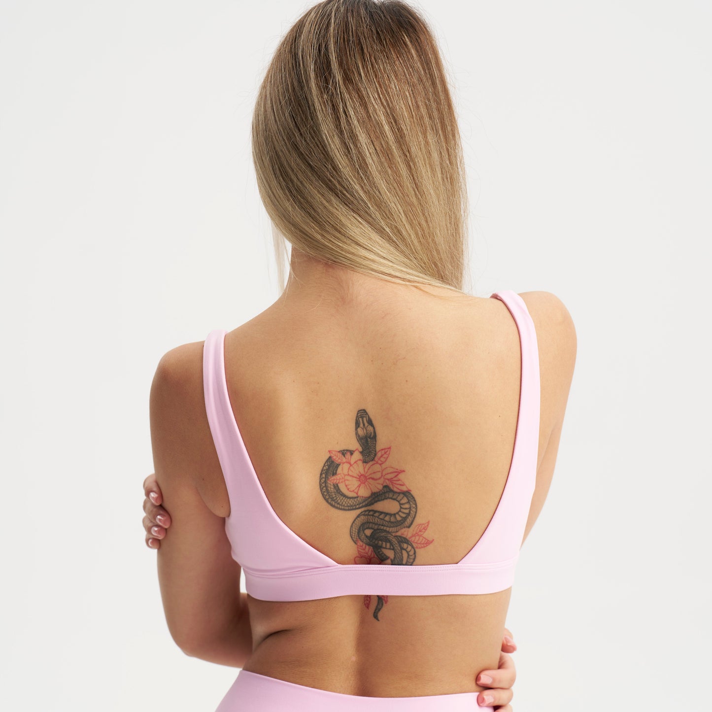 Woman wearing a pink sports bra and leggings with a tattoo on her back against a white background
